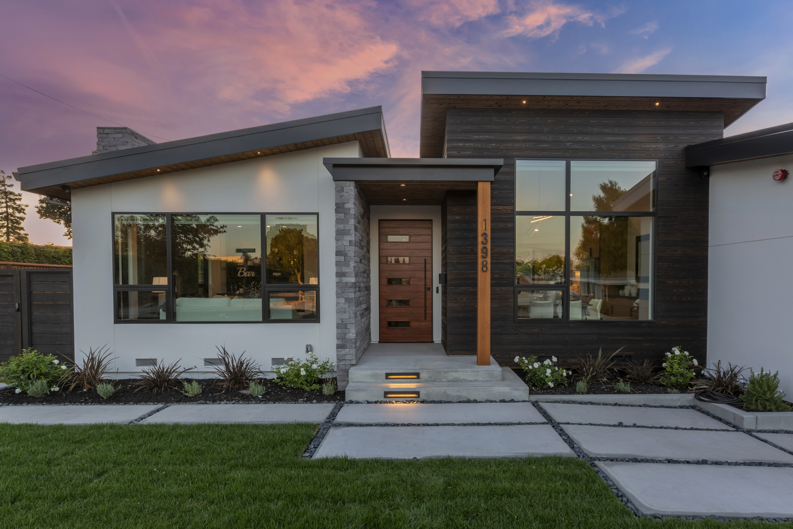 A modern home with grass and concrete steps leading to the front door.